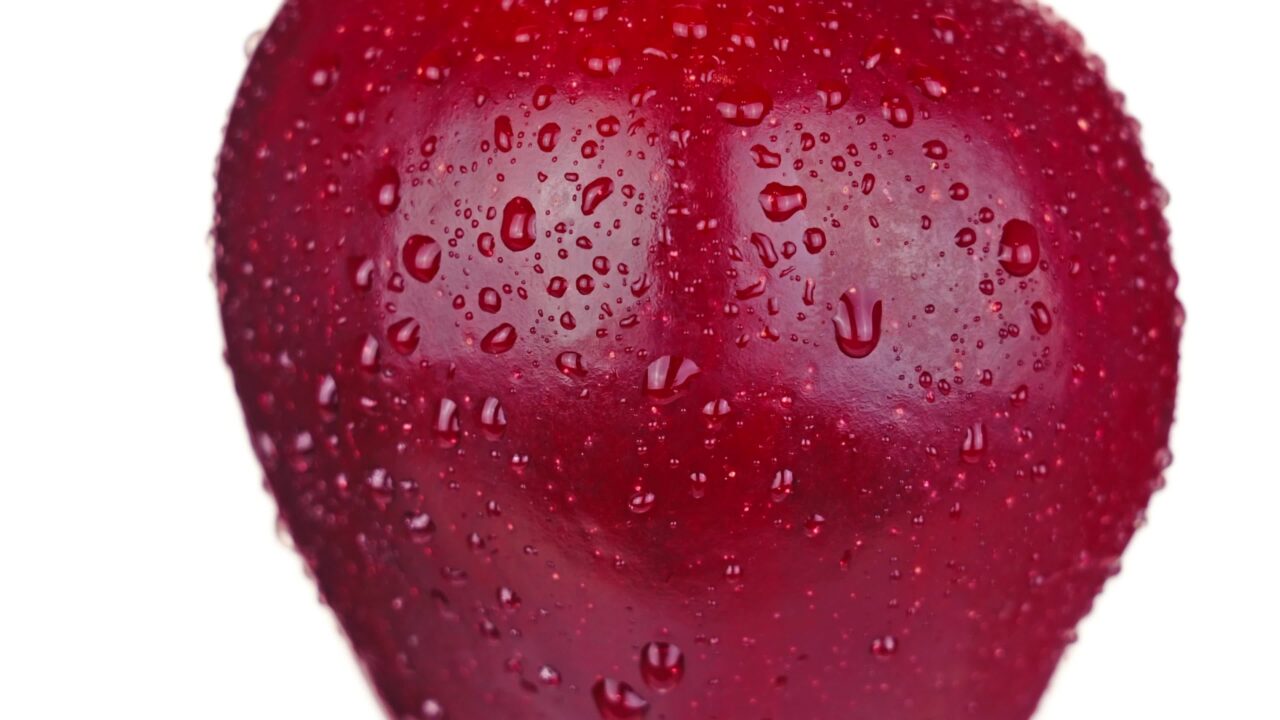La succosa mela rossa con gocce d’acqua gira il lato sinistro su bianco