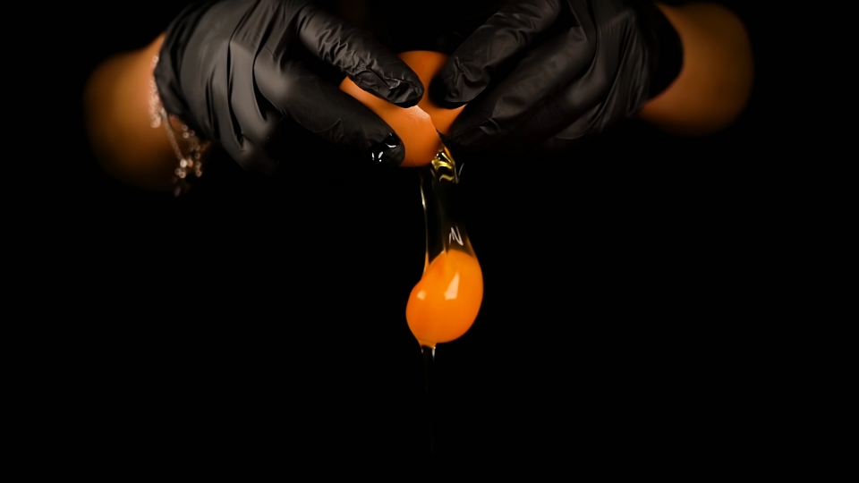 Le mani dell’uomo nei guanti rompono l’uovo cucinando un piatto gustoso sul nero