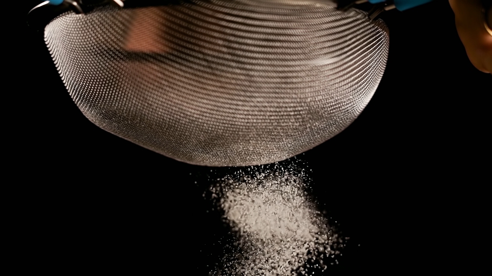 Baker sifts flour with metal sieve on black background