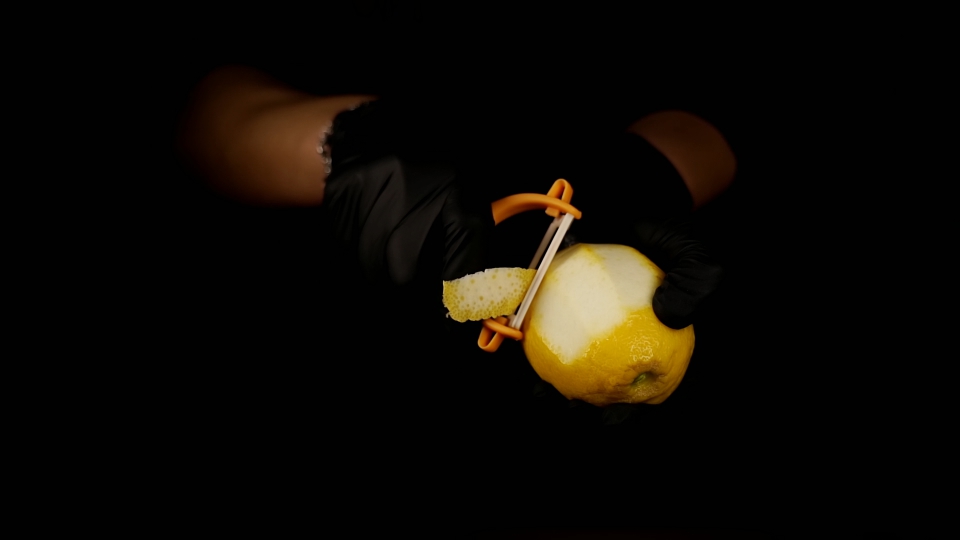 La persona taglia la scorza di limone con il pelapatate su sfondo nero