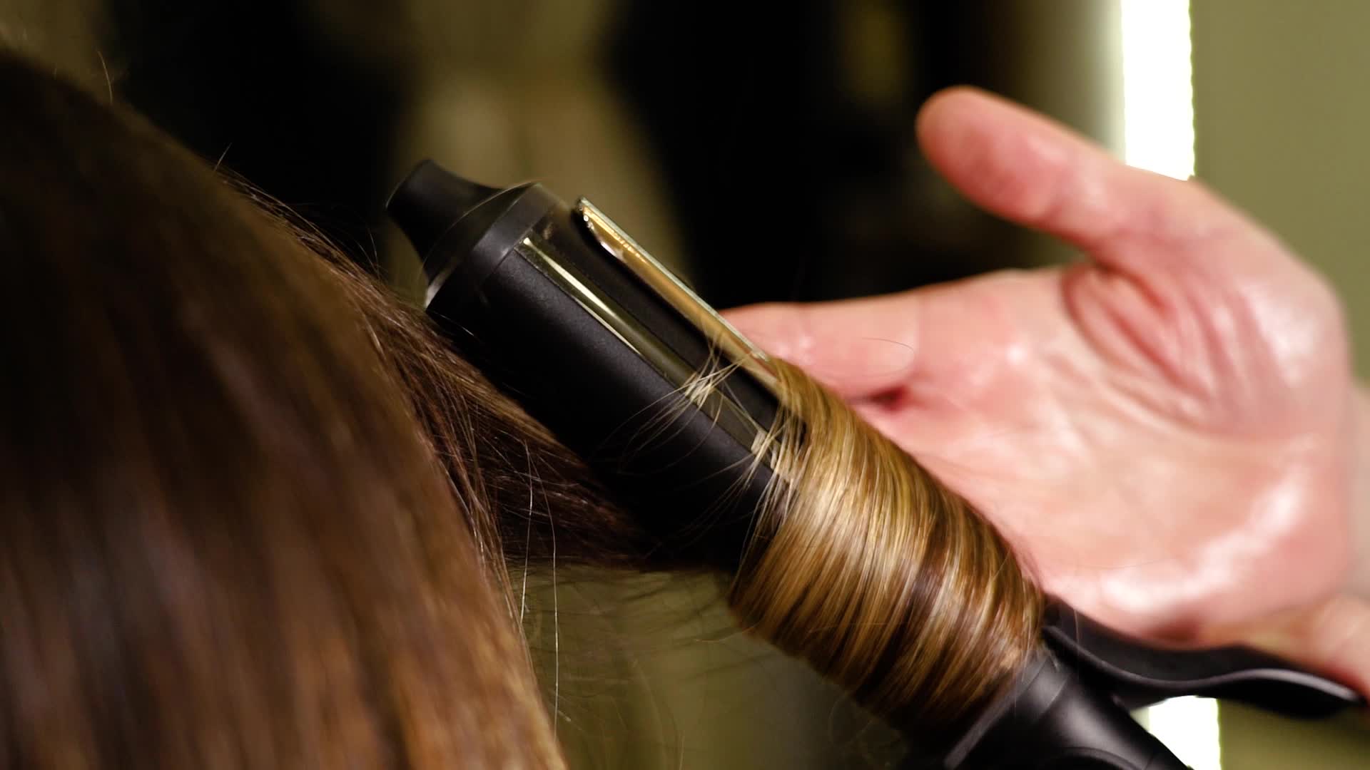 Hairdresser makes locks of client hair with curling iron