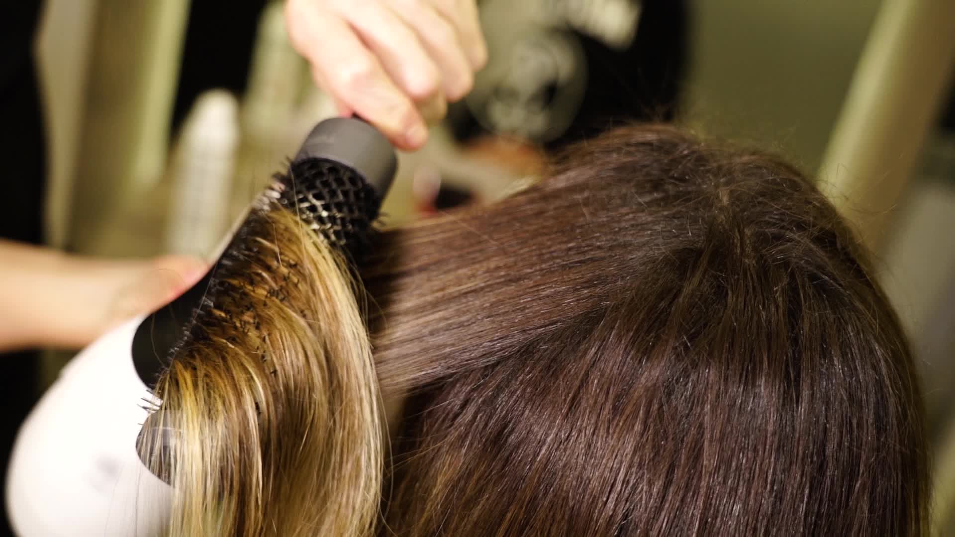 La donna raddrizza i capelli del cliente con la spazzola rotonda nel salone