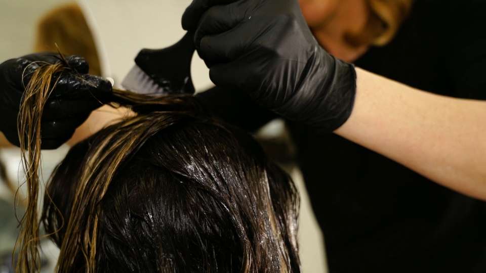 La donna in guanti applica la vernice sui capelli del cliente della signora con la spazzola