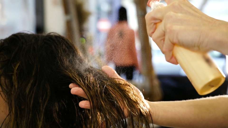 Hairdresser applies spray on woman wet hair lock in salon