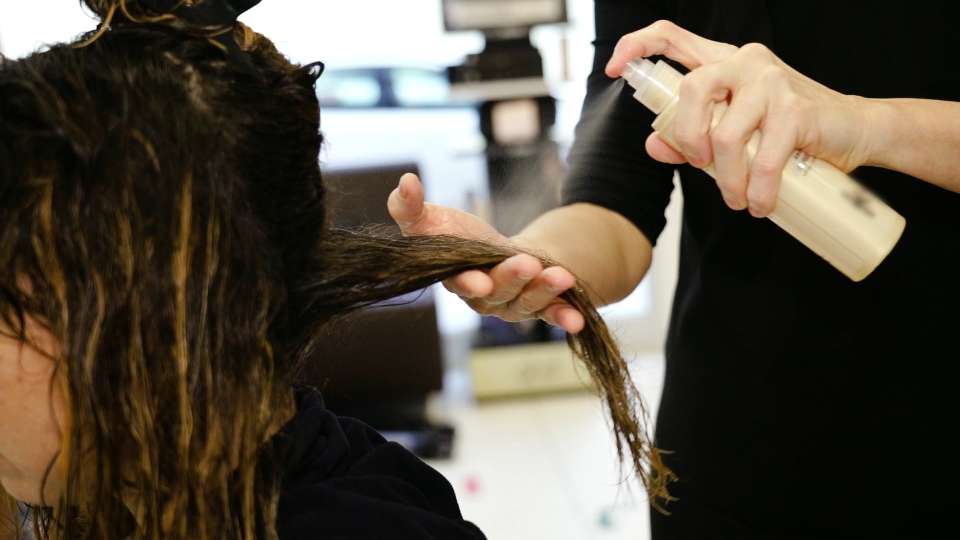 Il maestro applica lo spray sui capelli bagnati del cliente nel salone di bellezza