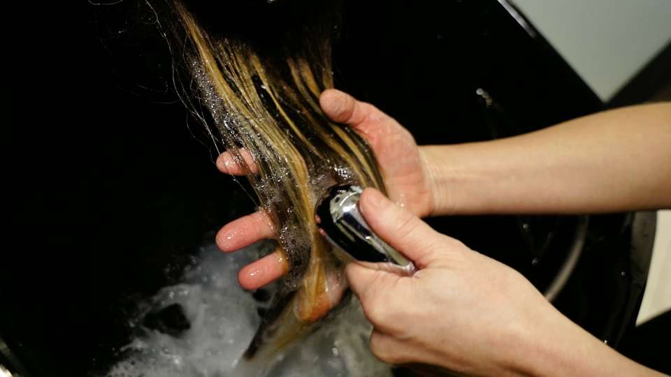 Hairdresser washes woman highlighted hair with running water