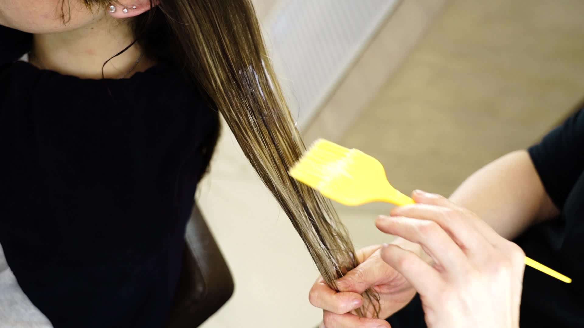 Hairdresser applies fixer on woman hair with yellow brush
