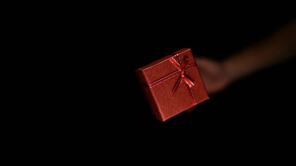 La mano della persona lancia verso l’alto una piccola scatola rossa di carta con il nastro