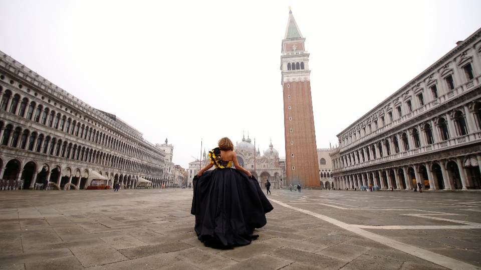 Woman walks along famous empty square holding dress plume