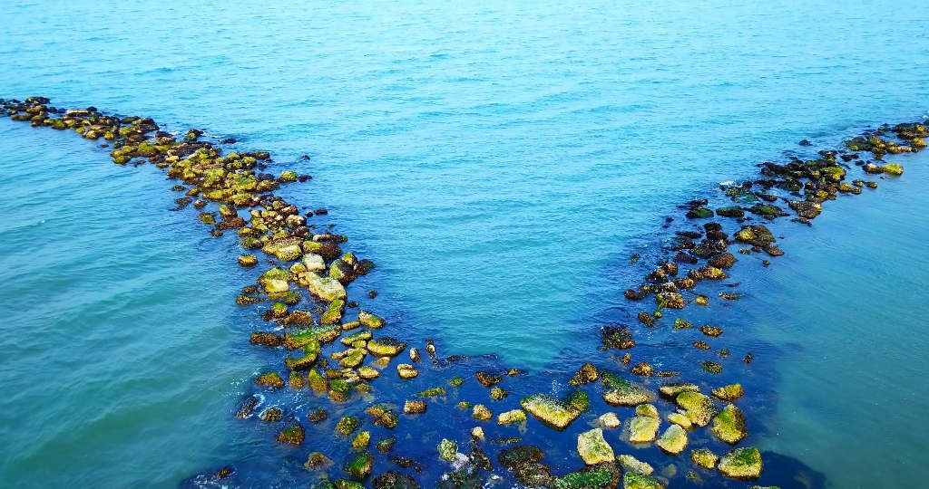 Artificial rock breakwater splits against endless blue sea
