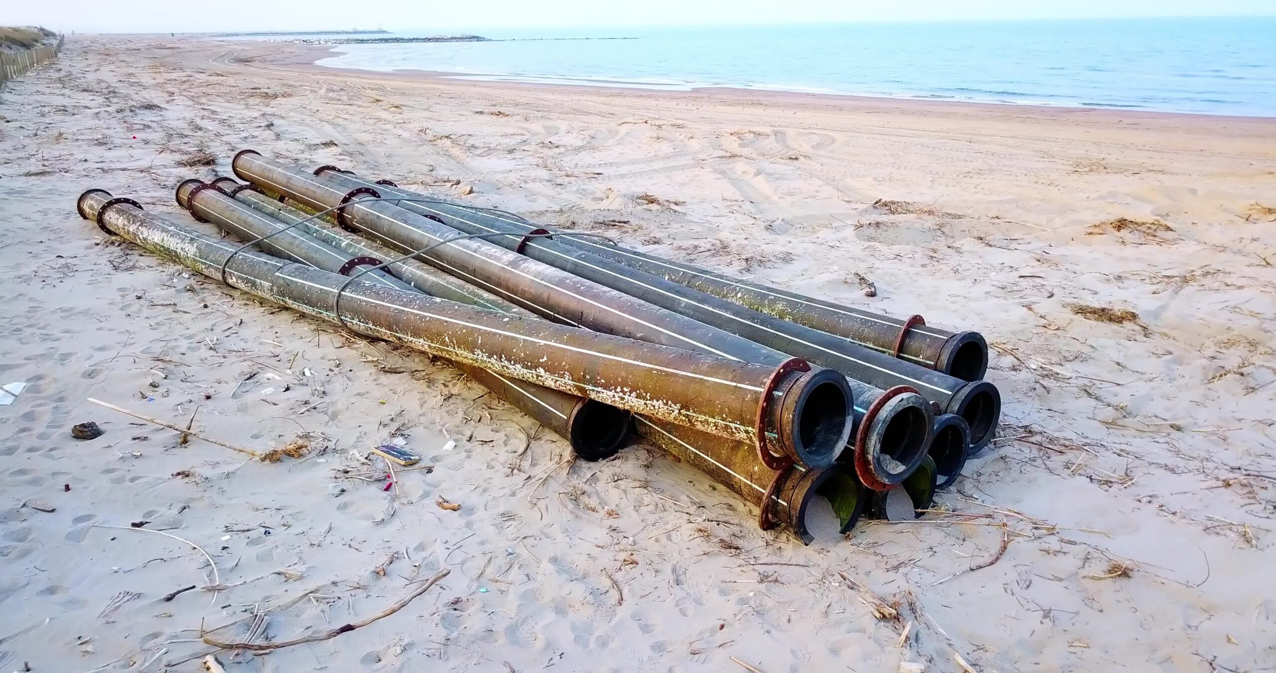 I tubi di metallo nero si trovano contro la recinzione sulla spiaggia con i rifiuti