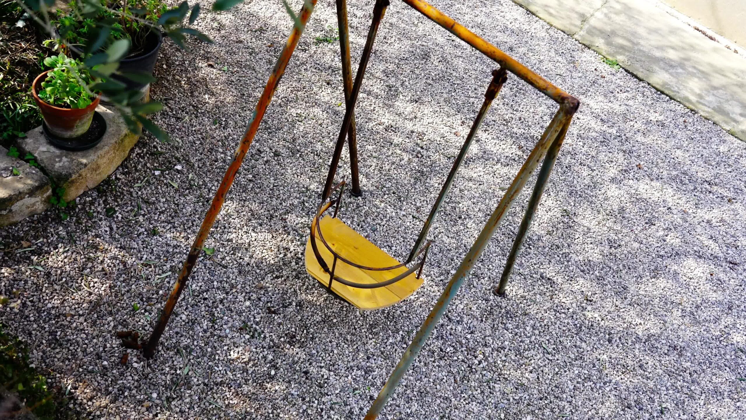 Piccola altalena gialla con elementi arrugginiti si trova in cortile