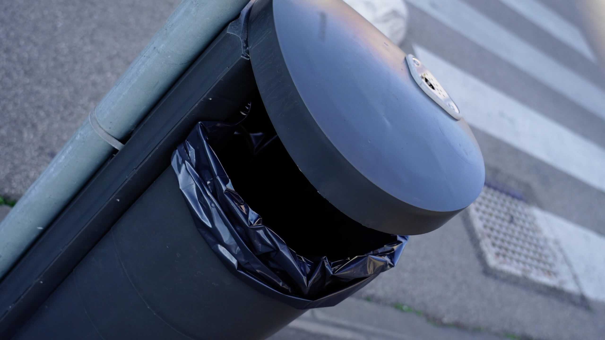 Bidone della spazzatura nero fissato sul palo grigio del lampione vicino alla strada