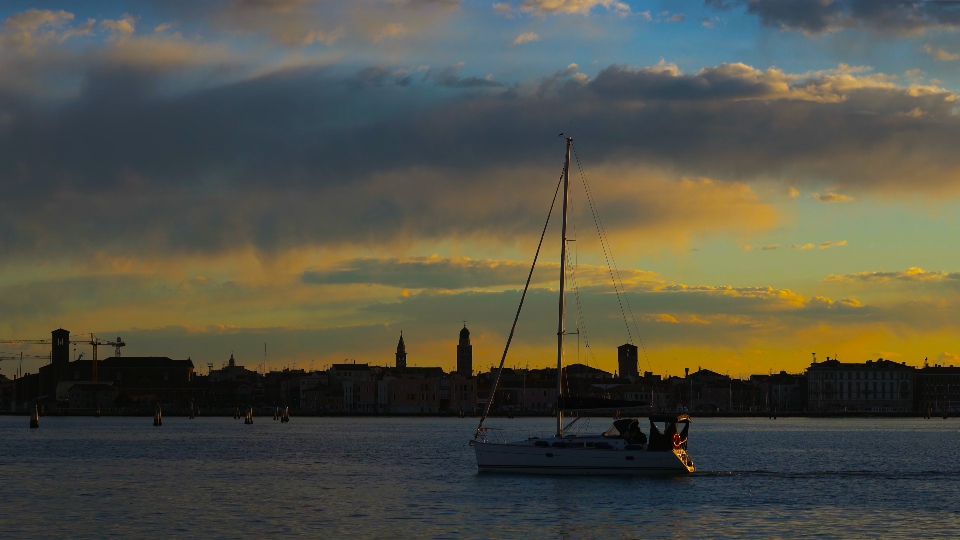 Boat sails on dark lagoon against historic city silhouette