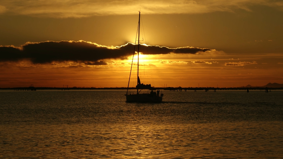 La barca con la vela sgonfia va alla deriva attraverso il brillante percorso della luce solare