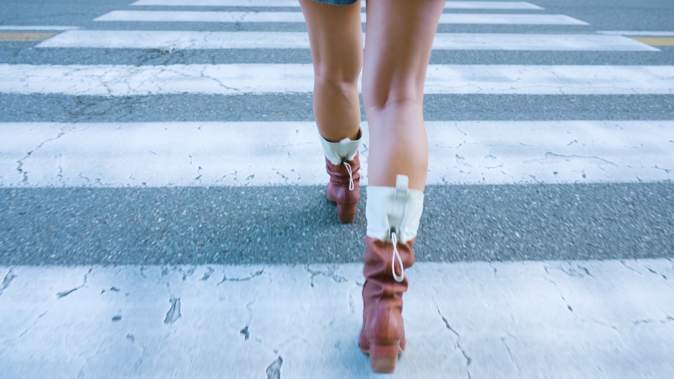 La donna in stivali attraversa la strada all’ampio passaggio pedonale