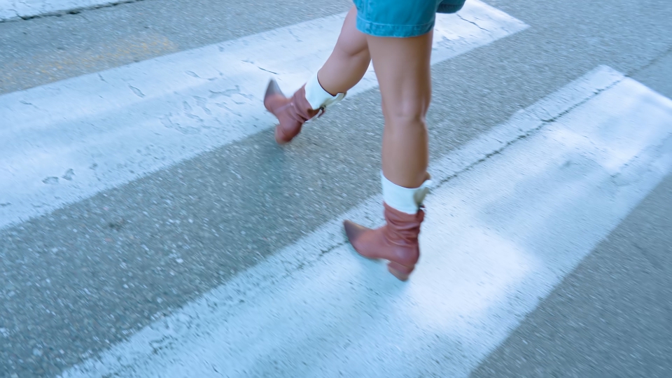 Signora pedone con stivali marroni attraversa la strada al passaggio pedonale