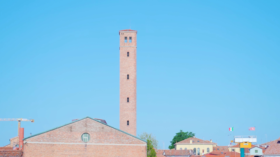 Alta torre in mattoni tra edifici a Murano sotto il cielo blu