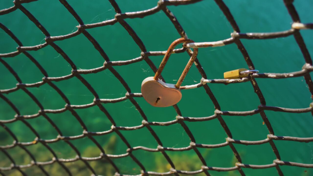 Heart-shaped lock hanging on iron grid against Bled lake