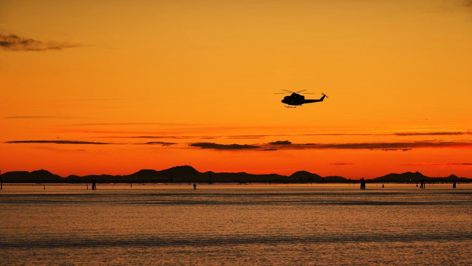 Dark silhouette of helicopter flies at sunset above river