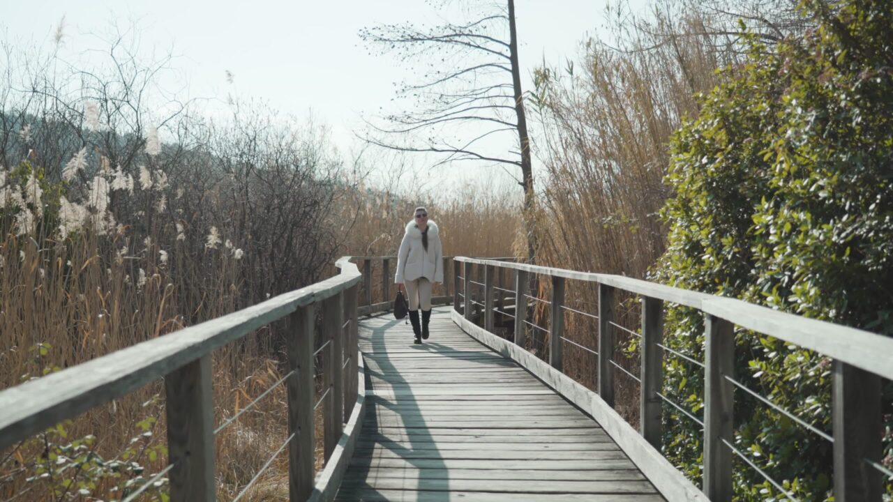 La donna cammina sulla passerella di legno nella soleggiata stagione autunnale