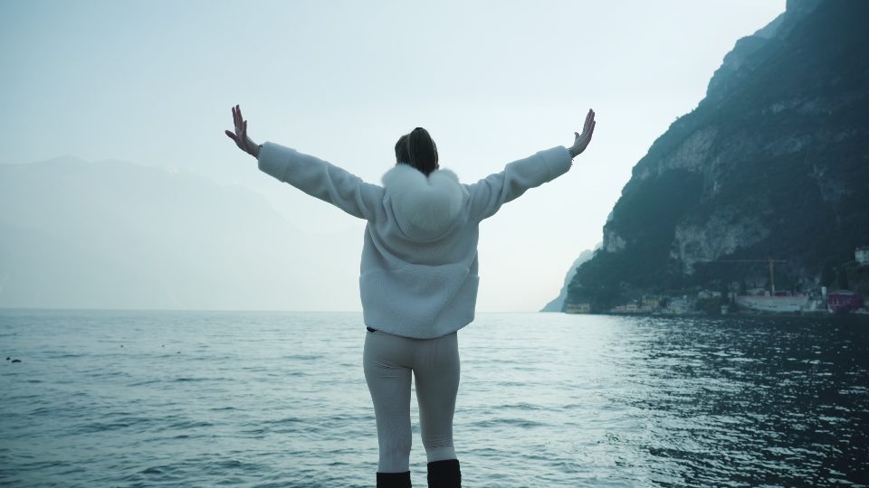 La donna alza le mani contro l’acqua luccicante nel lago di Garda