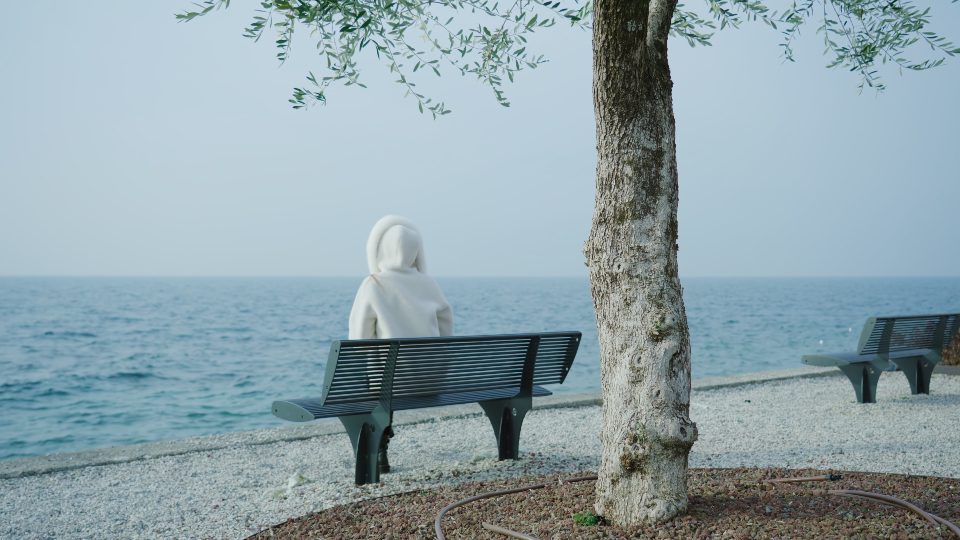 Donna si rilassa sulla panchina sull’argine guardando il lago di Garda