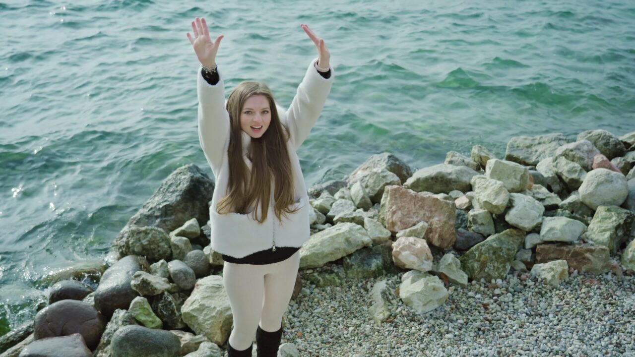 Donna felice alza le mani che catturano il vento sulla riva del lago