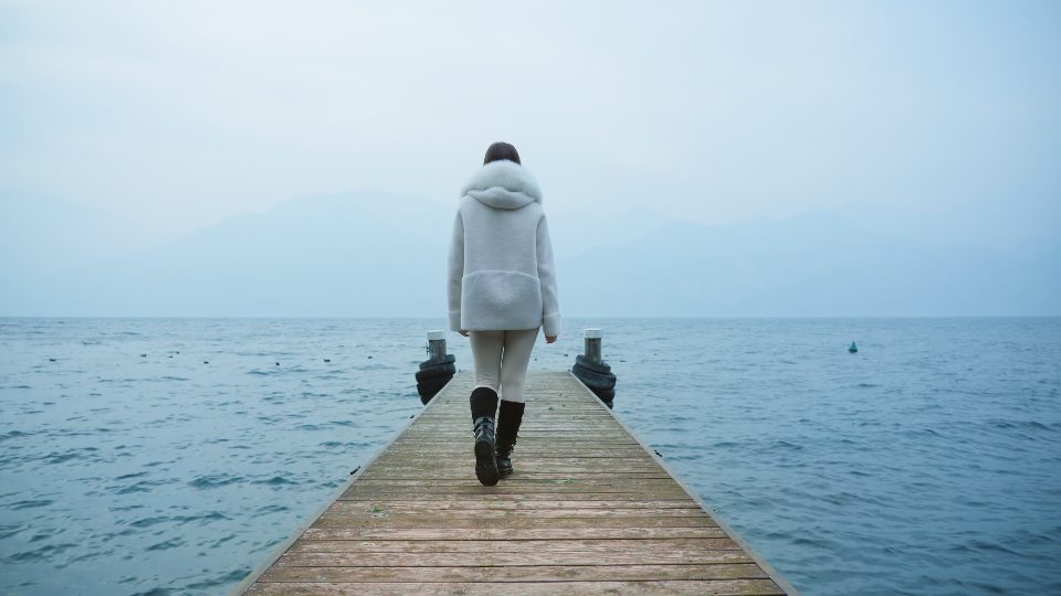 Donna cammina sul molo in legno godendo di viste sul lago di Garda