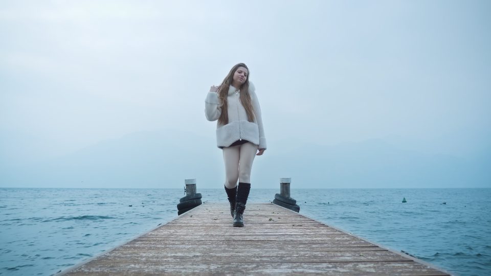 La donna con i capelli lunghi cammina sul molo di legno nel lago di Garda
