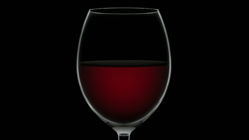 Empty goblet fills up with dessert wine on black background