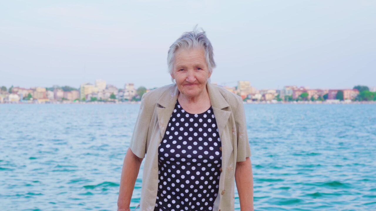 Elderly woman traveler strolls by waterside smiling widely