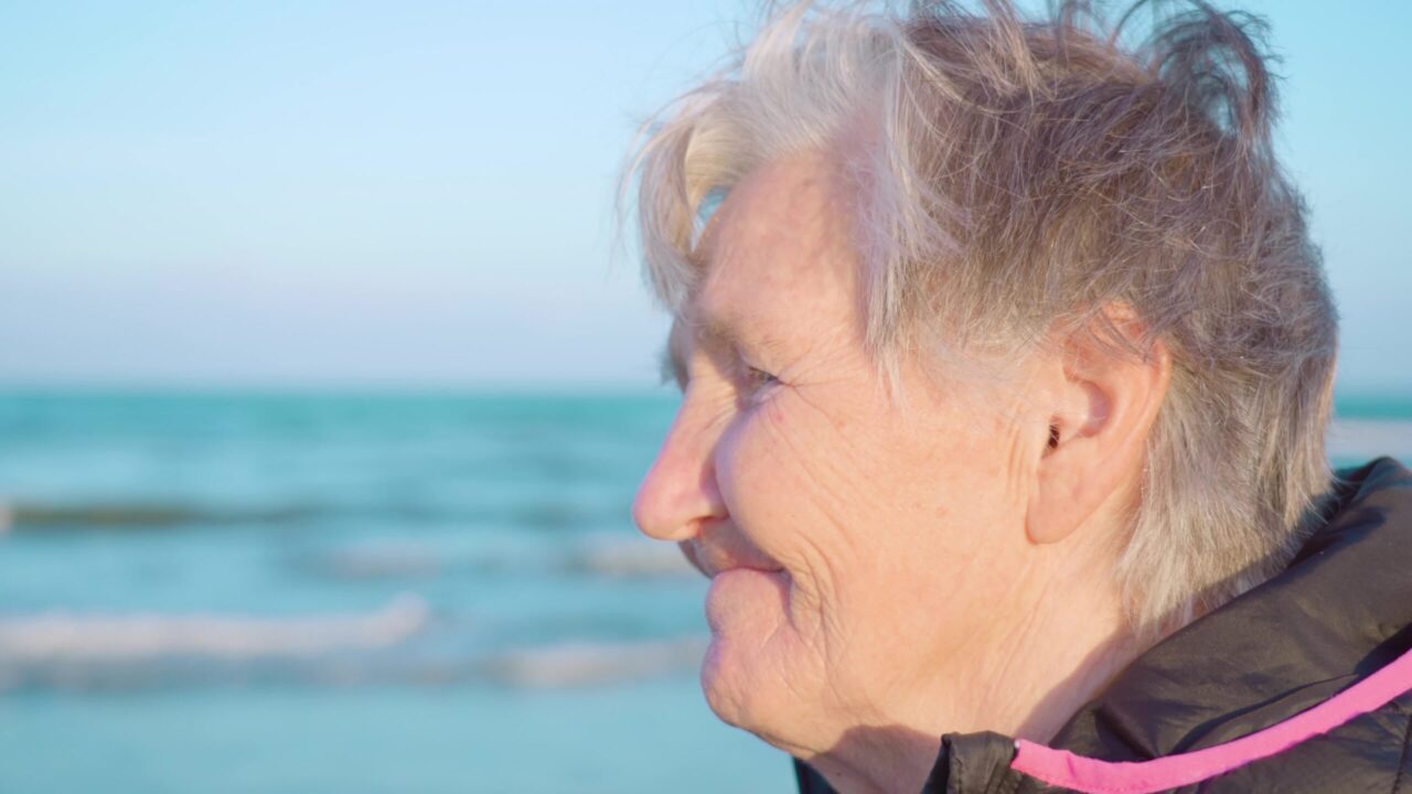 La viaggiatrice senior della donna con un taglio di capelli grigio corto in giacca a vento gode di una vista sul mare azzurro in piedi sulla spiaggia di Chioggia primo piano estremo