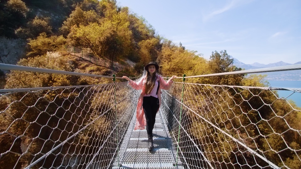 Woman walks on suspension bridge against lush yellowed trees