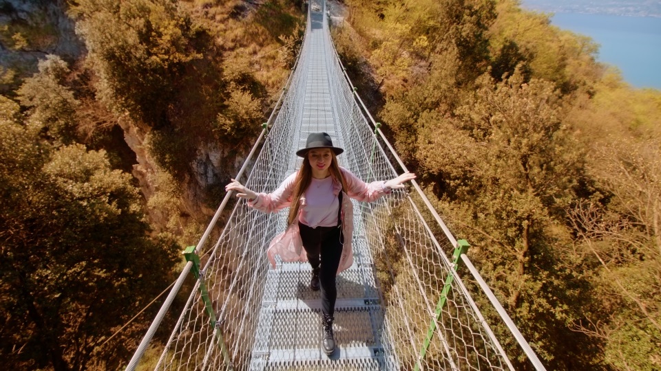 Lady tourist in hat walks on suspension bridge over gorge