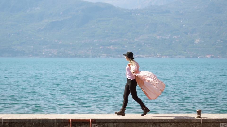 Cheerful woman enjoys walking on pier at Lake Garda dancing
