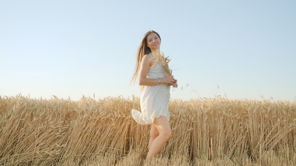 Blonde woman poses for photo standing in golden wheat field