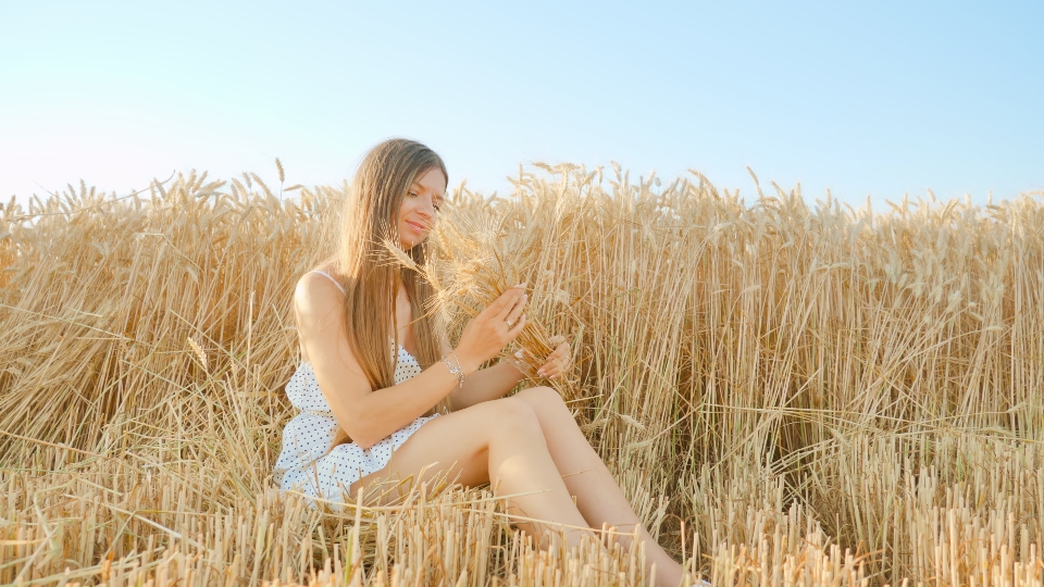 Woman sits in wheat field creating bouquet from spikelets