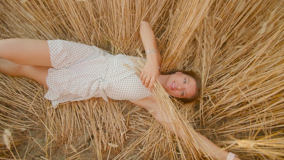 Happy woman in frock rests in flattened golden ripe field