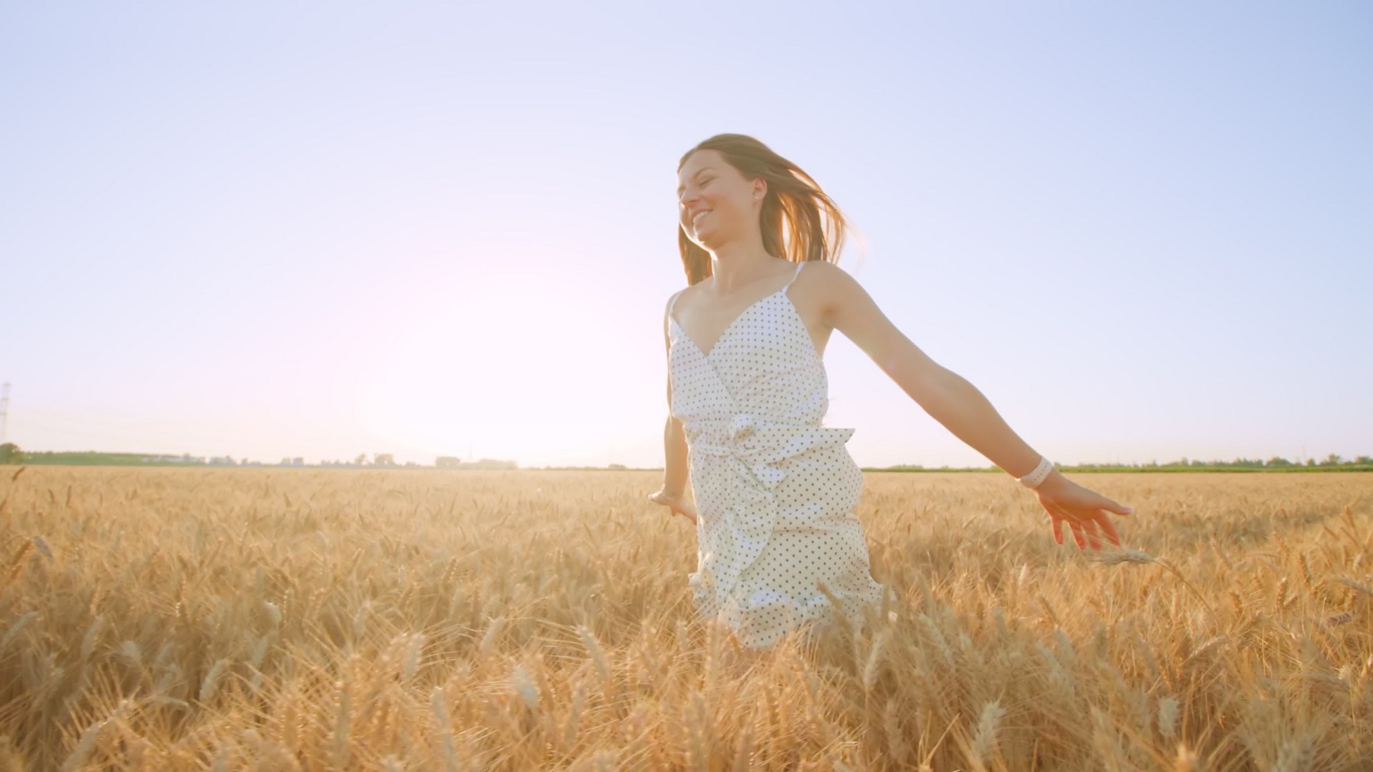 Cheerful woman runs in ripe wheat field under clear blue sky