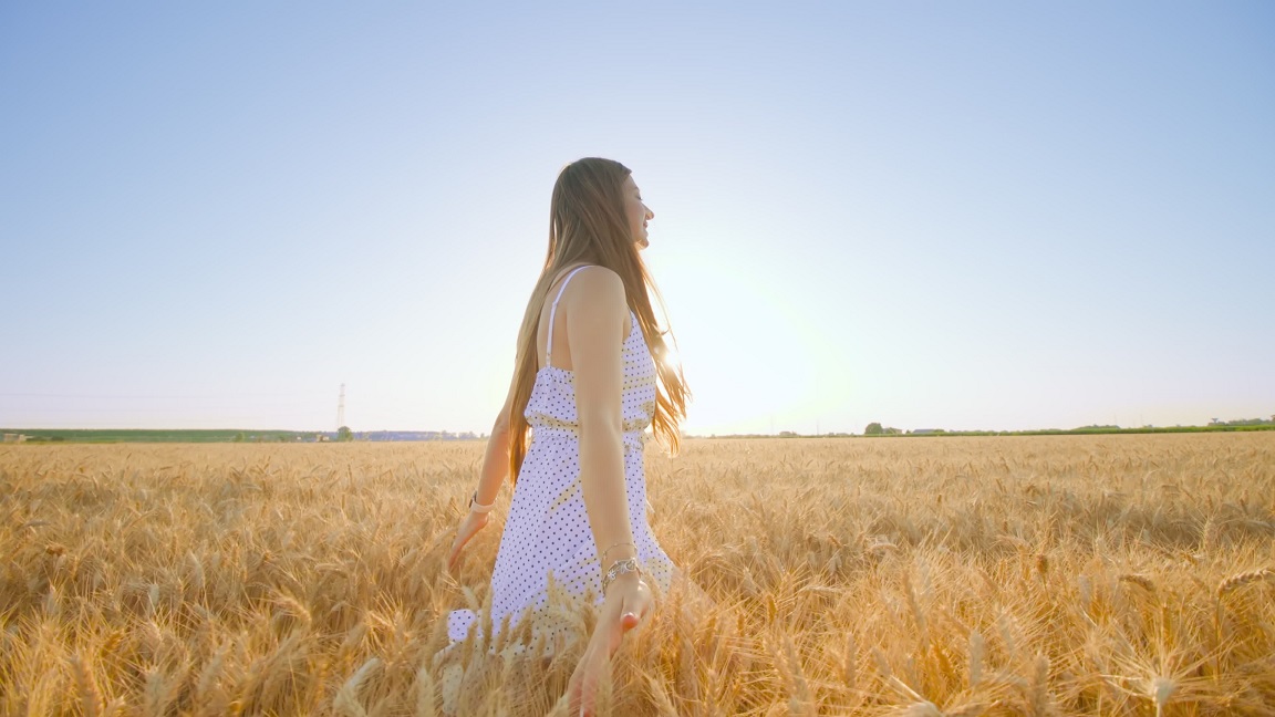 Long-haired woman in dress walks touching wheat spikelets