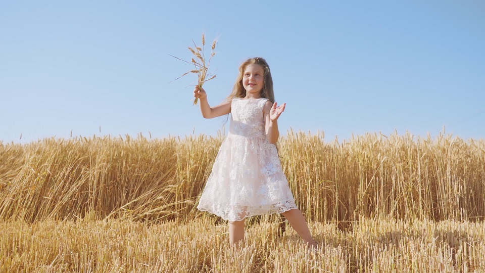 Cheerful girl dances in wheat field holding spikelet bouquet