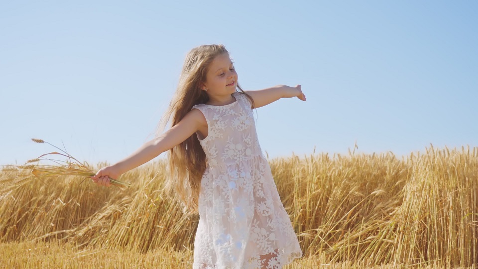 Cheerful girl has fun in ripe wheat field holding bouquet