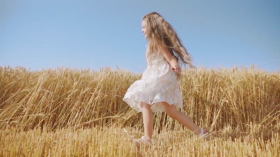 Cheerful girl with long loose hair runs in golden wheat field
