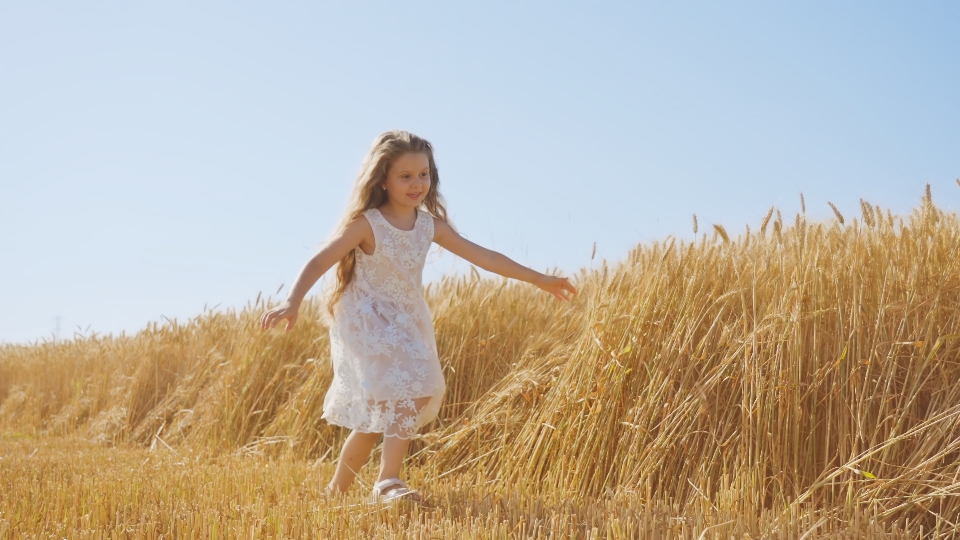 La bambina corre nel campo di grano toccando le spighette con la mano