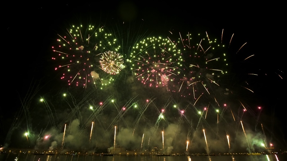 Colorful fireworks launched in air reflect on water surface