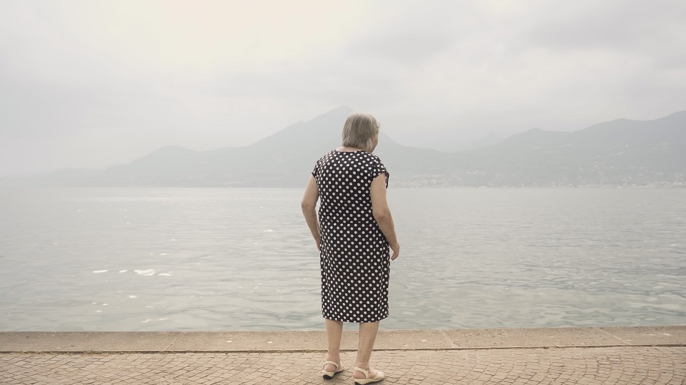 Elderly woman looks at Lake Garda against mountains in haze
