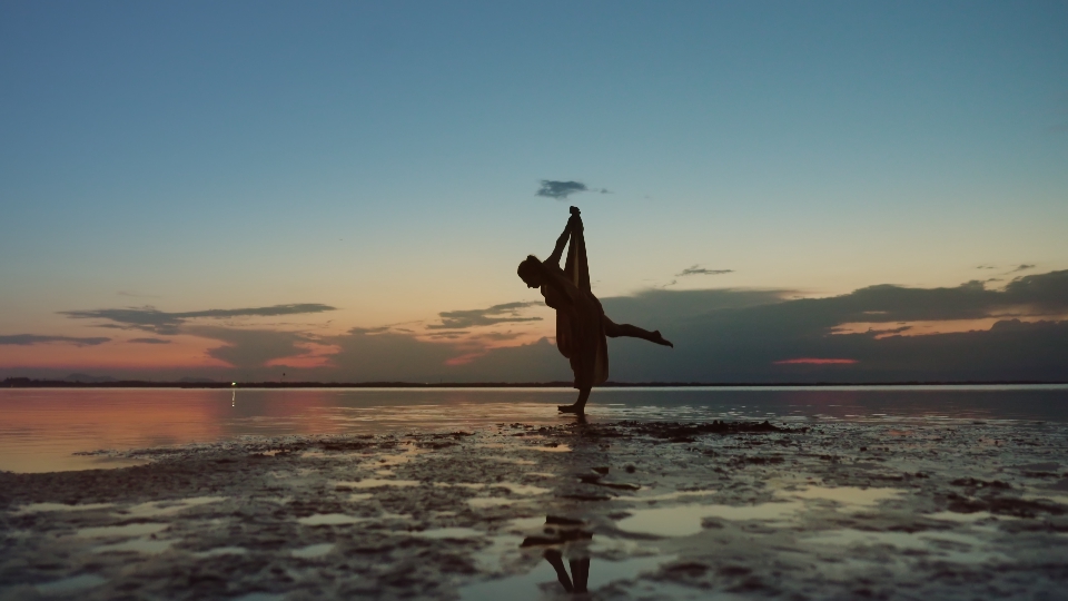 Dancer tries to get on a needle on the beach at sunset