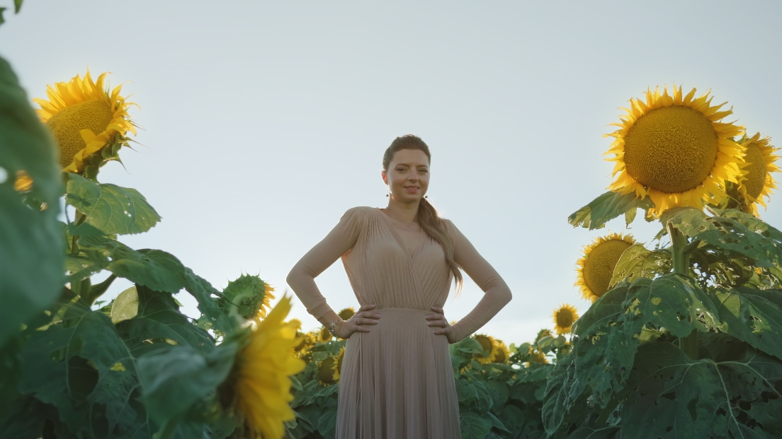 Elegant young woman standing among sunflowers in the sun