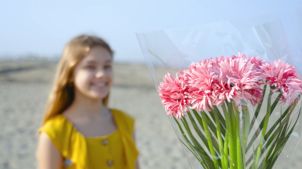 A bouquet of flowers in front of a girl who smiles in a fake way